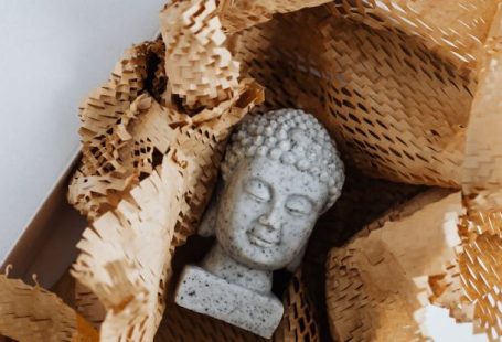 Online Safety - Top view of gray stone bust of Buddha placed on white marble table in cardboard box with craft perforated paper after receiving postal delivery