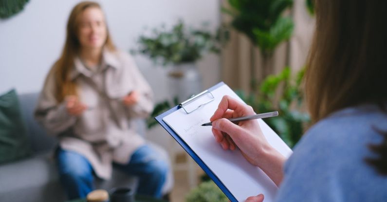 Moral Dilemmas - Unrecognizable professional female psychologist writing on clipboard while sitting against client on blurred background during psychotherapy session in light office